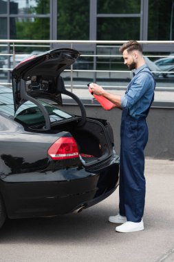 Side view of mechanic looking at canister of windshield washer fluid near car  clipart