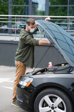 Dışarıda koruyucu maskeli bir adam arabanın kaputunu açıyor. 