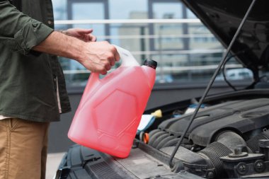 Cropped view of driver holding canister with windshield washer fluid near blurred car  clipart