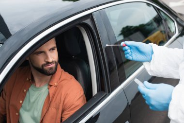 Medical worker holding cotton swab of pcr test near driver in car  clipart