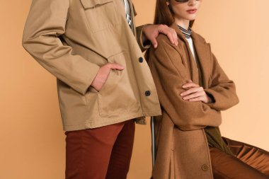 cropped view of man touching shoulder of stylish woman while standing with hand in pocket isolated on beige