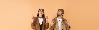 stylish couple in autumn outfit pointing up with fingers isolated on beige, banner