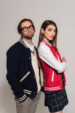 young woman in stylish jackets looking at camera while posing near man isolated on grey