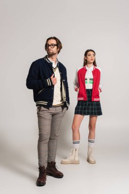 full length view of trendy couple in jackets and leather boots posing on grey background