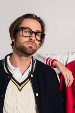 stylish man in eyeglasses looking at camera near woman leaning on his shoulder isolated on grey