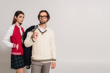 woman with hand in pocket of stylish jacket near man in white sweater isolated on grey