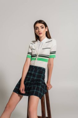 pretty woman in striped polo t-shirt and plaid skirt looking at camera on grey background