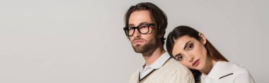 young woman leaning on back of man in stylish eyeglasses isolated on grey, banner