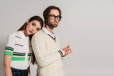 young woman leaning on back of man in white knitted jumper isolated on grey