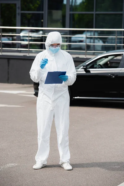 Trabajador Médico Con Traje Materiales Peligrosos Sujetando Portapapeles Cerca Automóvil —  Fotos de Stock