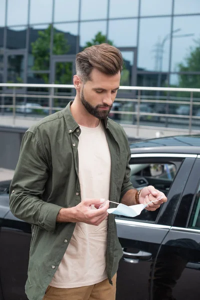 Hombre Joven Sosteniendo Máscara Médica Cerca Coche Aire Libre —  Fotos de Stock