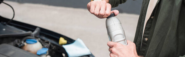 Cropped view of man opening bottle of engine oil near car, banner 