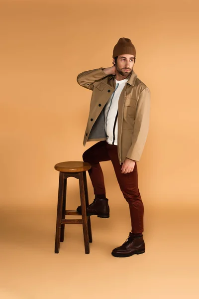 Young Man Fashionable Clothes Looking Away While Posing Wooden Stool — Fotografia de Stock