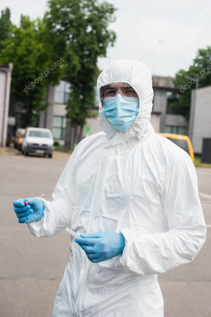 Medical worker in hazmat suit holding pcr test outdoors 