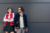 young couple in trendy jackets looking at each other near grey wall