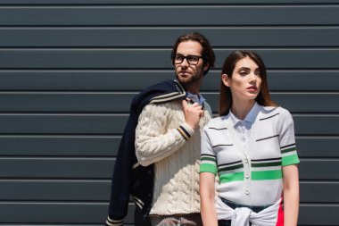 trendy couple in stylish clothes standing near grey wall outdoors