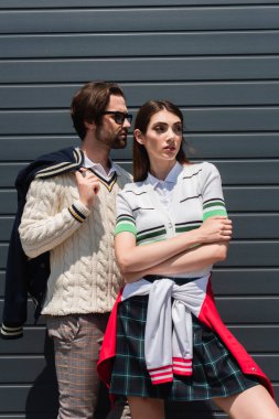 young couple in fashionable clothes looking away while posing outdoors