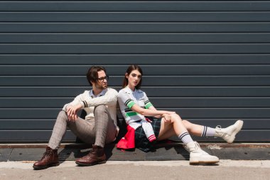 young fashionable couple sitting on border near grey wall outdoors