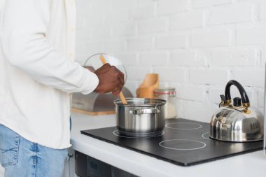 Afro-Amerikalı genç bir adamın mutfakta yemek pişirmesi. 