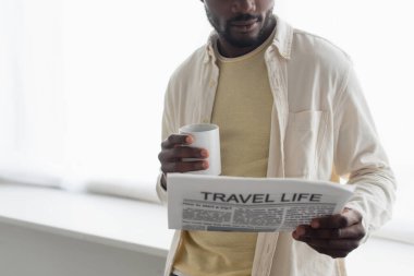 Afro-Amerikan bir adamın elinde bir fincan kahve tutarken ve seyahat hayatı gazetesi okurken çekilmiş görüntüsü. 