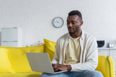 Afrikalı Amerikalı serbest yazar sarı koltukta otururken dizüstü bilgisayarda yazıyor.