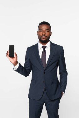 Takım elbiseli Afro-Amerikan iş adamı elinde gri ekranda boş ekranlı akıllı telefon tutuyor.