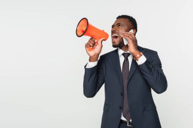 Afro-Amerikan iş adamı takım elbiseli, megafonla bağırıyor ve griler üzerinde izole bir şekilde akıllı telefondan konuşuyor.