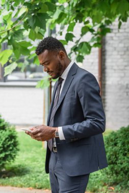 Takım elbiseli Afrikalı Amerikalı iş adamı cep telefonundan mesaj yolluyor. 