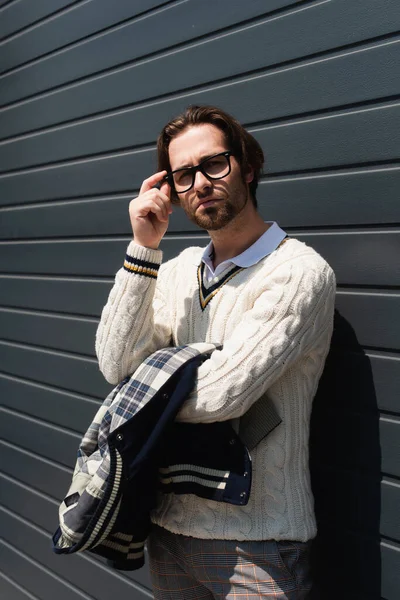Trendy Man White Knitted Sweater Adjusting Eyeglasses Grey Wall Outdoors — Foto de Stock