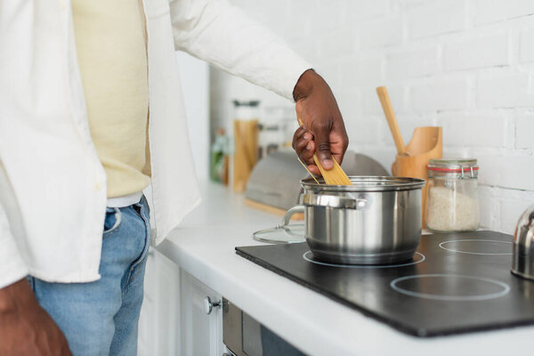cropped view of young african american man cooking spaghetti in kitchen
