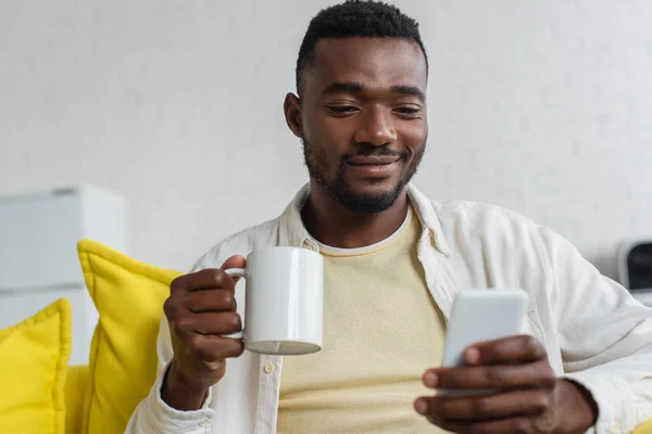 Sonriente Joven Afroamericano Hombre Usando Teléfono Celular Sosteniendo Taza — Foto de Stock