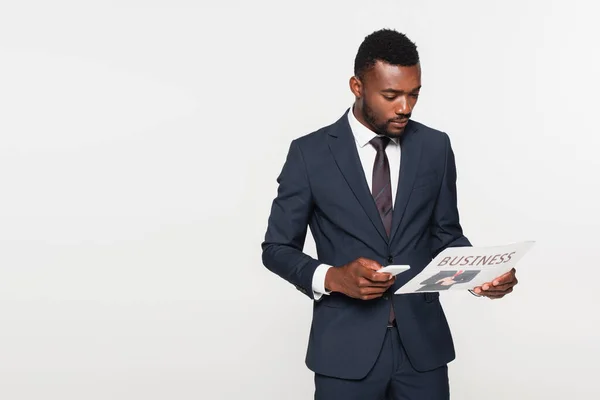Αφροαμερικάνος Επιχειρηματίας Κοστούμι Κρατώντας Smartphone Ενώ Διαβάζοντας Εφημερίδα Απομονωμένη Γκρι — Φωτογραφία Αρχείου