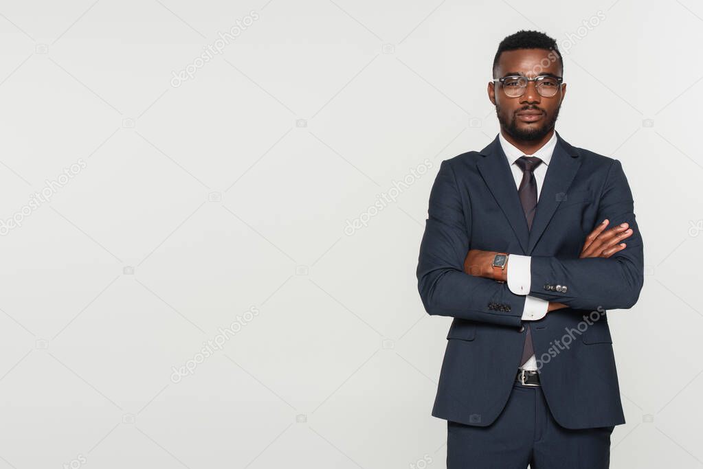 african american man in eyeglasses standing with crossed arms isolated on grey