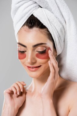 Kafasında havlu olan gülümseyen genç bir kadın gri renge göz bandı yapıştırıyor.