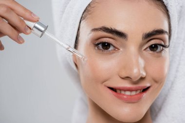 Gri üzerine izole edilmiş pipetle nemlendirici serum uygulayan mutlu genç bir kadın.