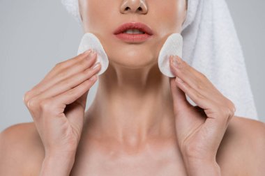 Gri üzerine izole edilmiş pamuk pedlerle makyaj yapan genç bir kadının görüntüsü.