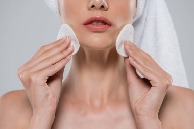 cropped view of young woman removing makeup with cotton pads isolated on grey clipart
