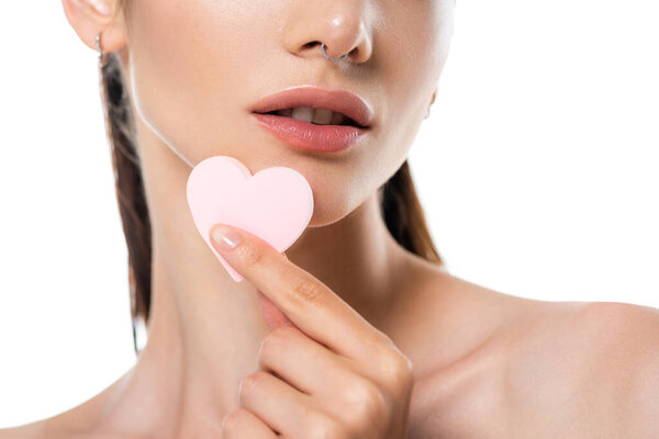 частичный вид женщины с проколотым плечом, держащей губку в форме сердца, изолированную на белом 