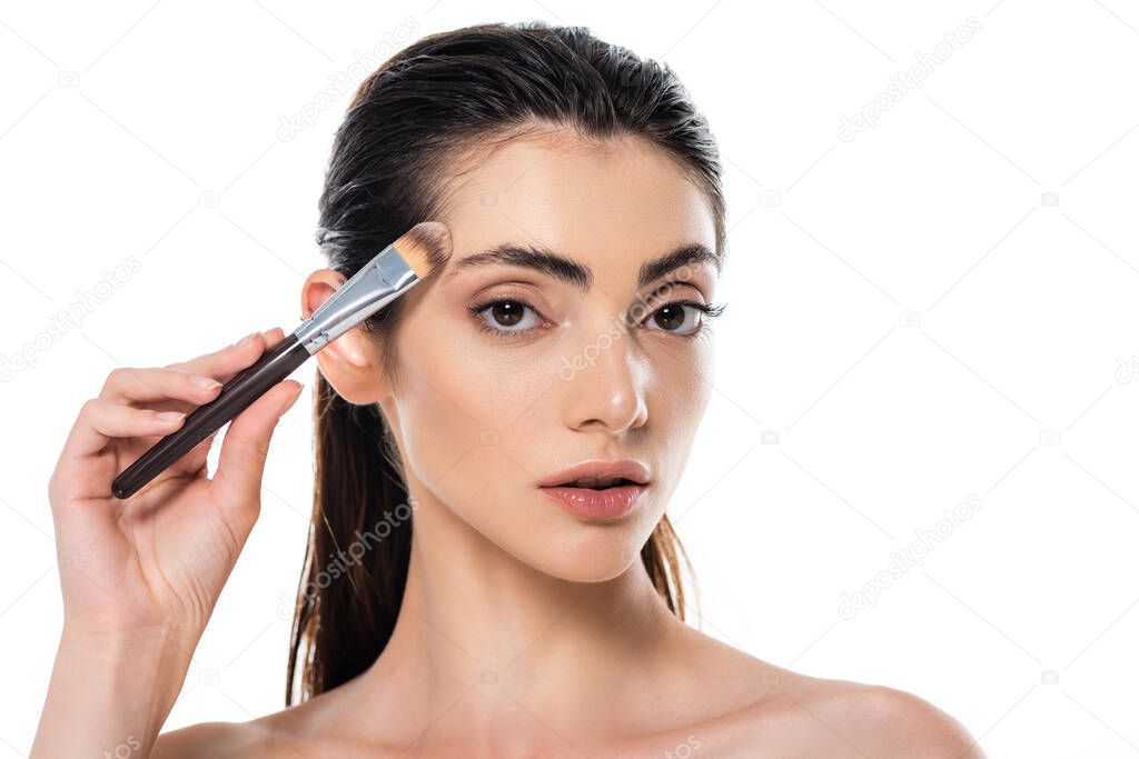 brunette woman applying face foundation with cosmetic brush isolated on white