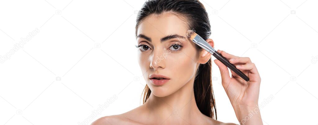 brunette woman applying face foundation with cosmetic brush isolated on white, banner