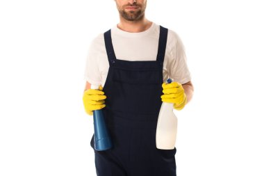 Cropped view of cleaner in overalls holding bottles of detergents isolated on white  clipart
