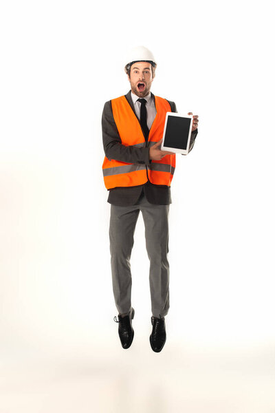 Amazed engineer holding digital tablet while jumping isolated on white 