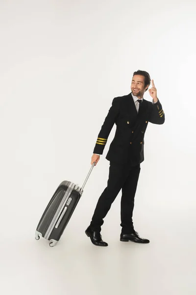笑顔パイロットとともにスーツケースポインティングとともに指上の白い背景 — ストック写真