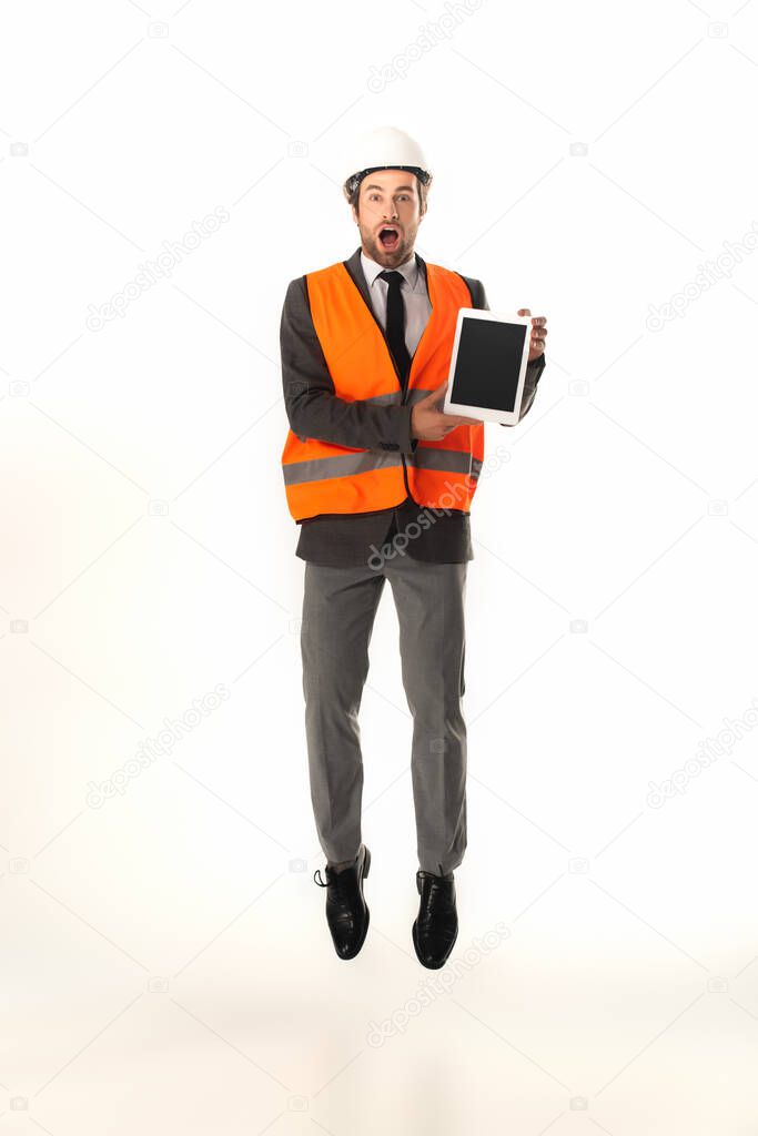 Amazed engineer holding digital tablet while jumping isolated on white 