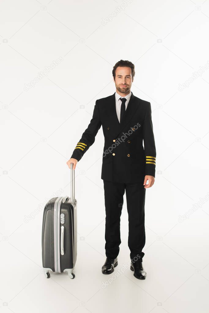 Young pilot with suitcase standing on white background 