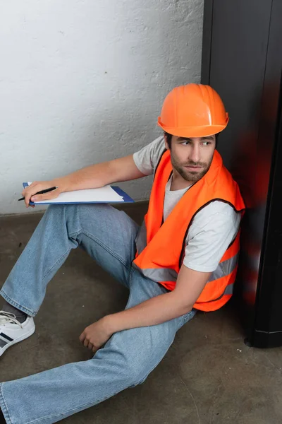 Junger Arbeiter Mit Klemmbrett Sitzt Auf Dem Boden — Stockfoto