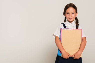 Elinde fotokopi kitapları tutarken kameraya bakan mutlu okul çocuğu.