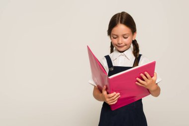 Okul üniformalı gülümseyen kız, gri üzerine izole edilmiş defter okuyor.