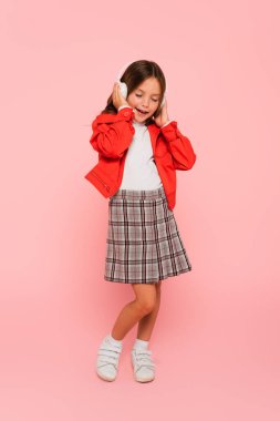 Şık giyinmiş neşeli çocuk pembe gözleri kapalı müzik dinliyor.