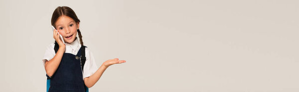 позитивный школьник указывая рукой во время разговора на смартфоне изолированы на серый, баннер